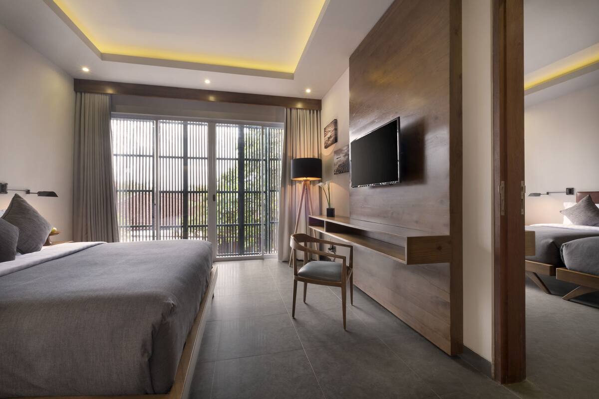 Une chambre d’hôtel moderne dotée d’un grand lit, d’un bureau, d’une chaise, d’un téléviseur fixé au mur et d’un balcon avec des rideaux.