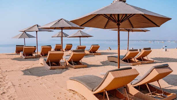 Une plage bordée de rangées de chaises longues en osier et de grands parasols, disposés pour permettre aux gens de prendre un bain de soleil.