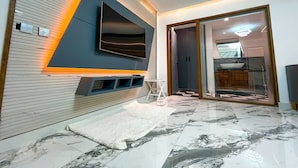 Una sala de estar moderna con un televisor de pantalla plana grande montado en la pared, un manto mullido blanco y un suelo de mármol con diseño.