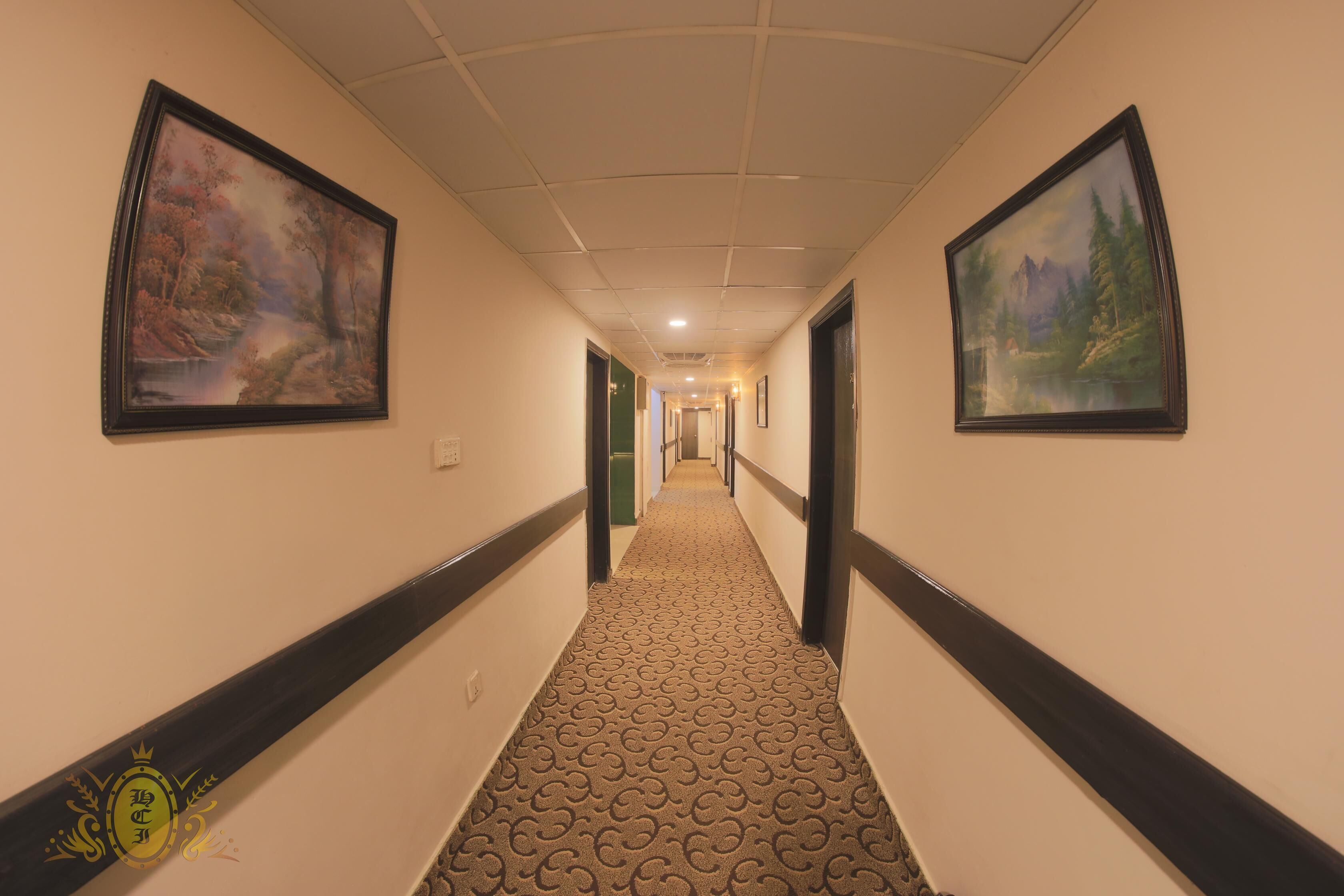 A hotel hallway with patterned carpet, black and white walls, and framed landscape paintings.