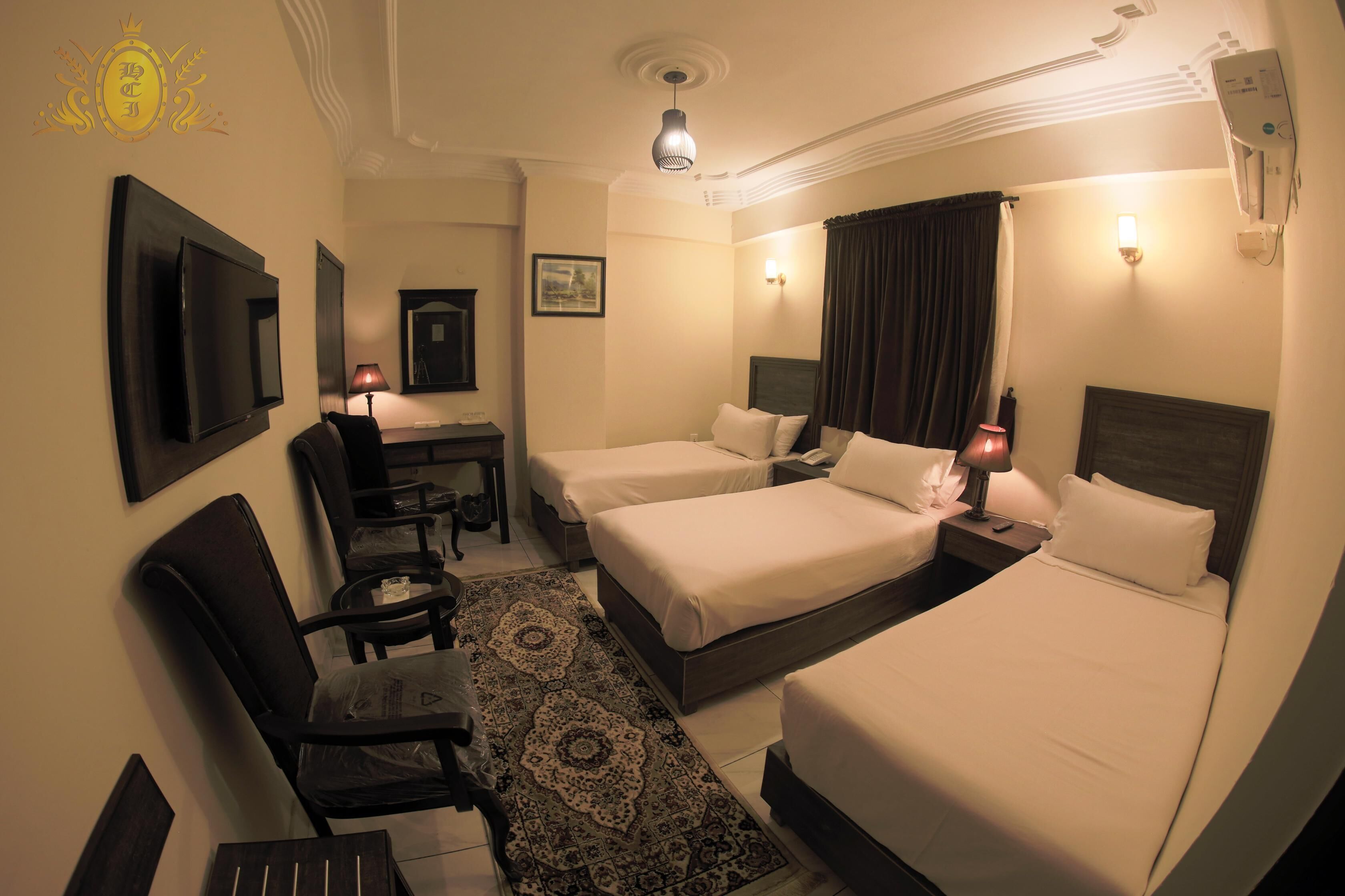A hotel room with two beds, a desk, a chair, a TV, and a patterned rug.