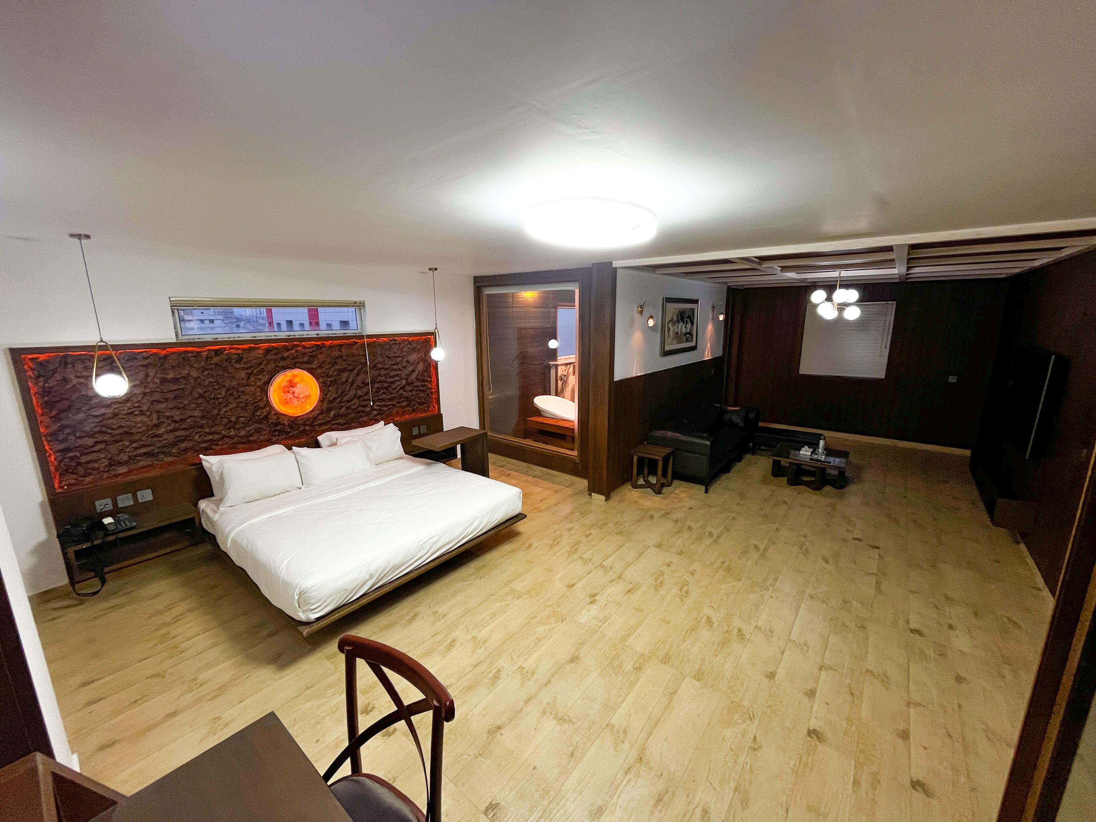 Ett hotellrum med en säng, ett skrivbord, en stol, en tv och ett badrum som syns genom en glasdörr.