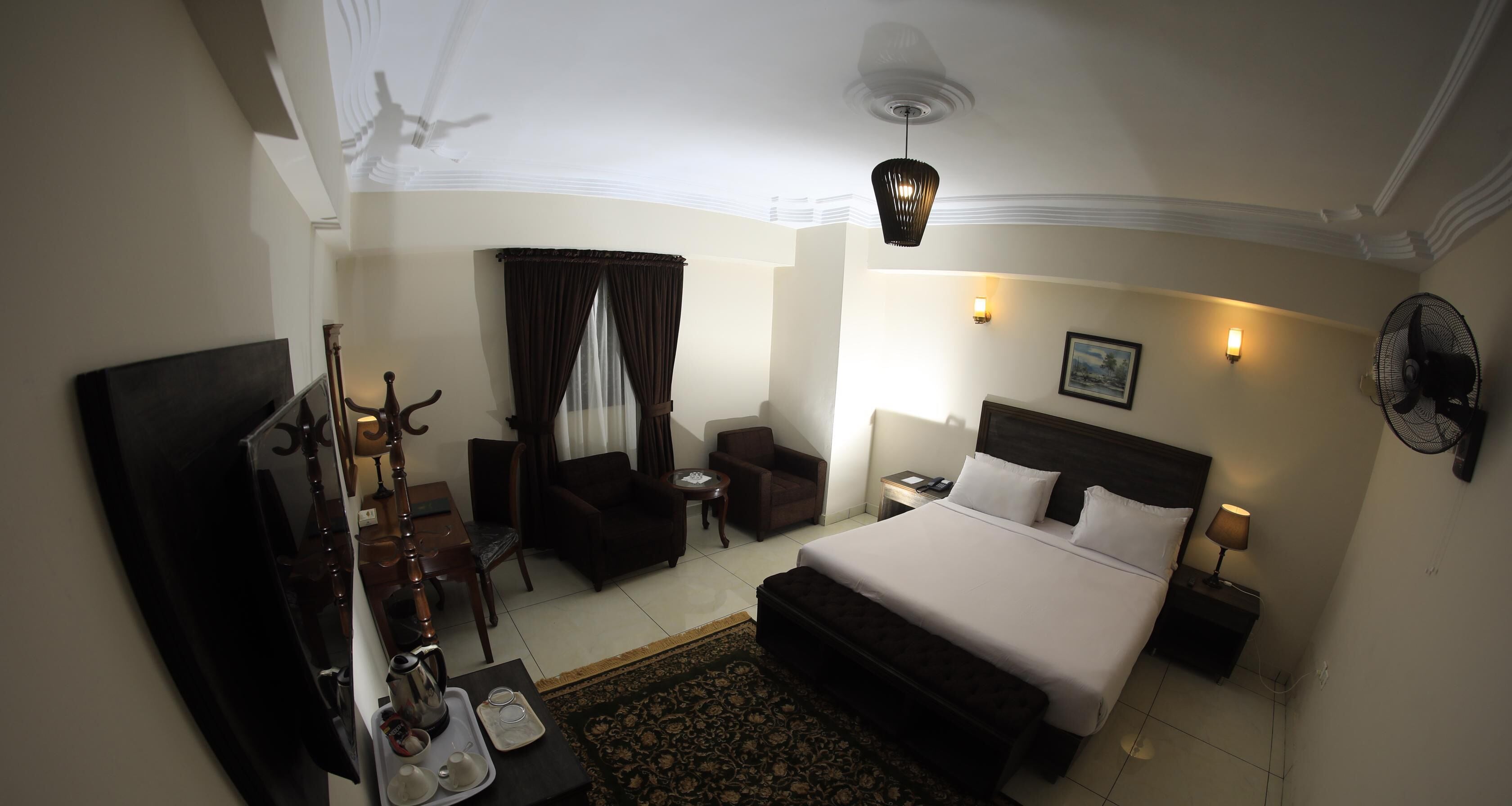 A hotel room with a large bed, a desk with a chair, a small table, and a sofa.