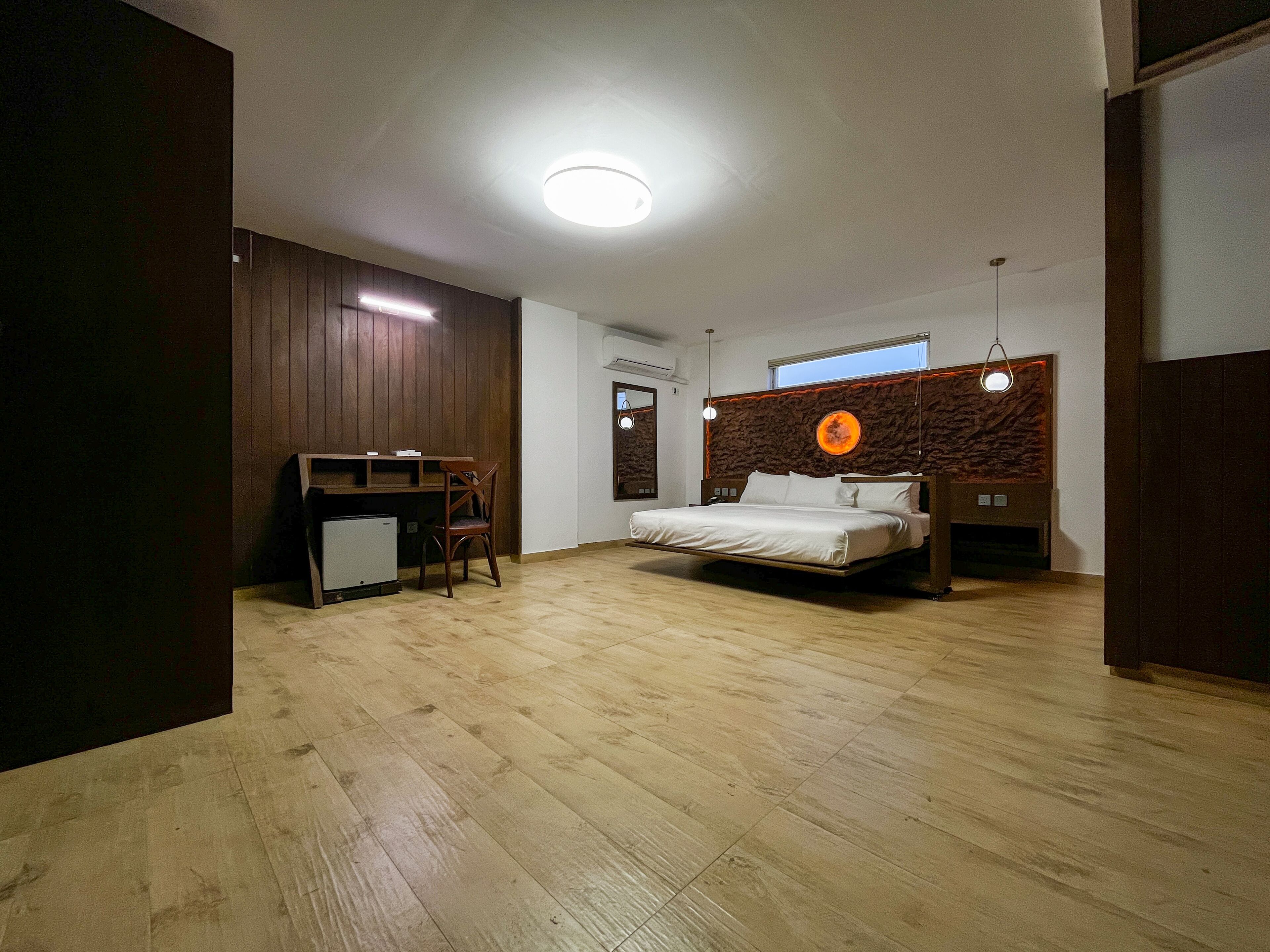 A modern bedroom with a wooden floor, a bed with a unique headboard, a desk, and a chair.