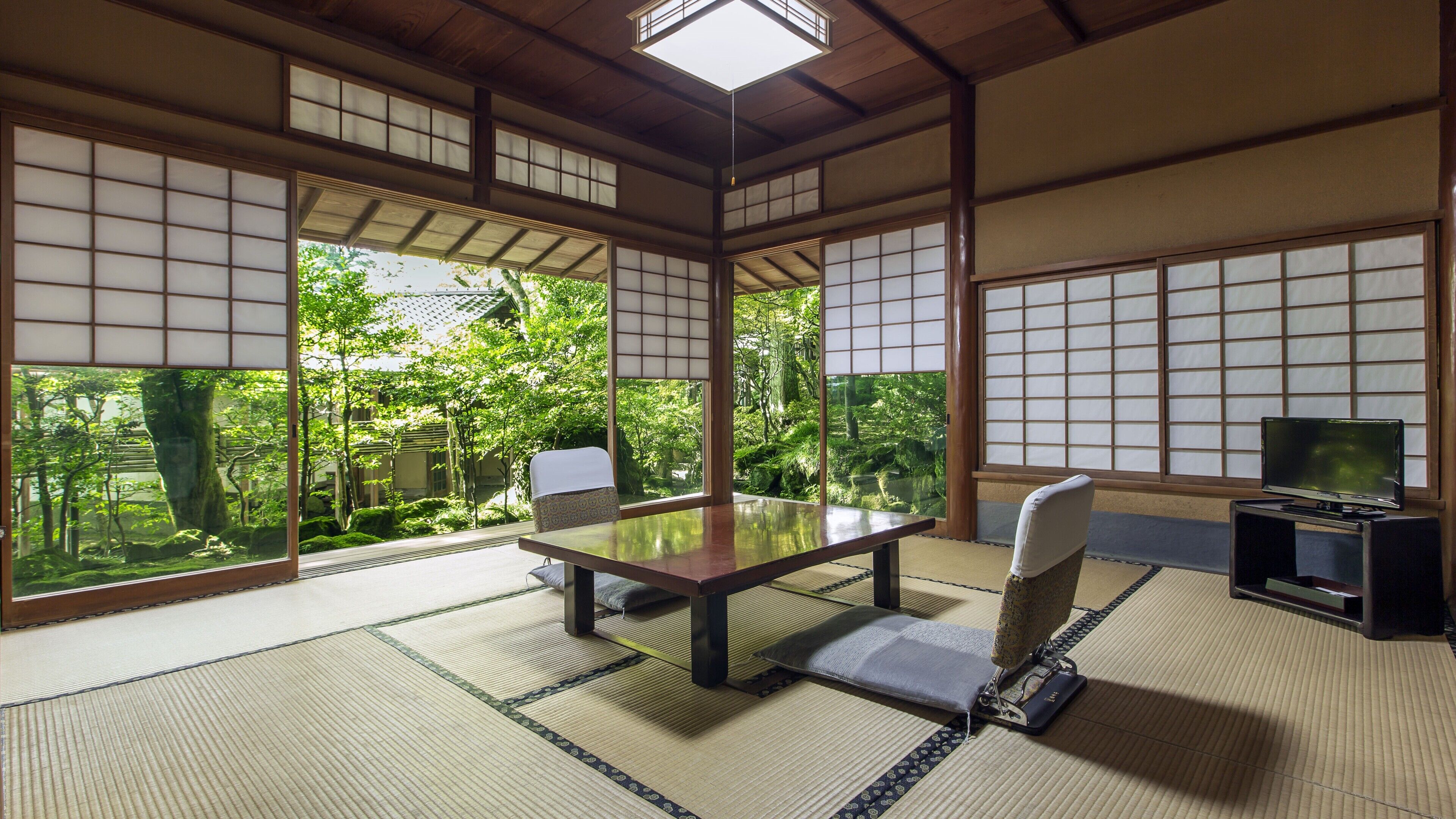 A traditional Japanese room with tatami flooring, a low table, a cushioned chair, and a television.
