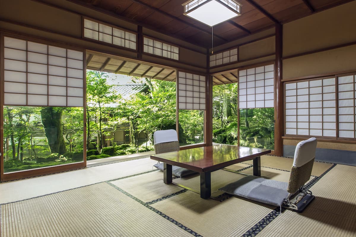 A traditional Japanese room with tatami flooring, a low table, a cushioned chair, and a television.