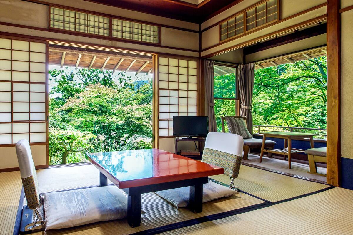 A traditional Japanese room with tatami flooring, a low table, a chair, and a television.
