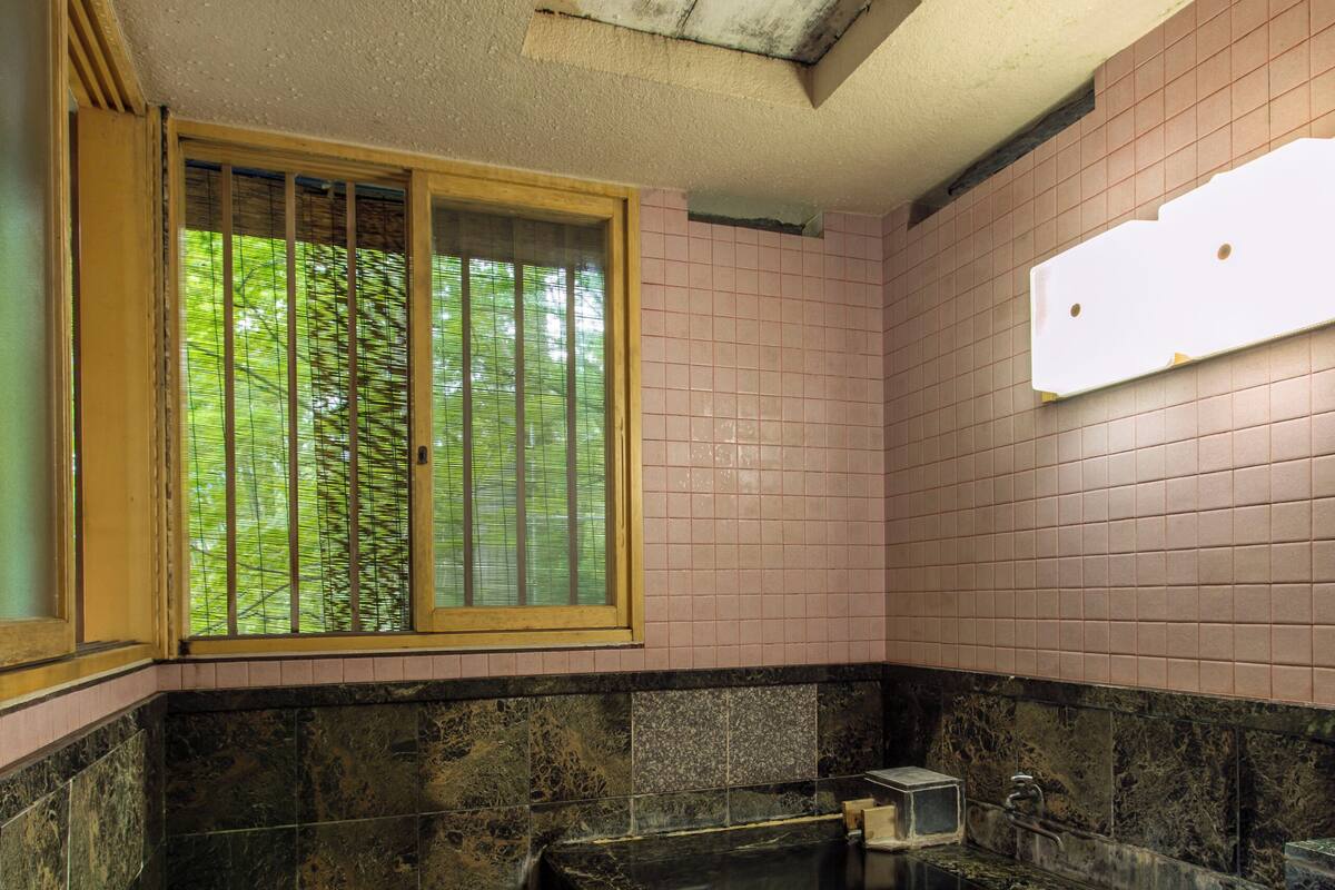 A bathroom with a stone floor, a bathtub, a window with bars, and a wooden stool.