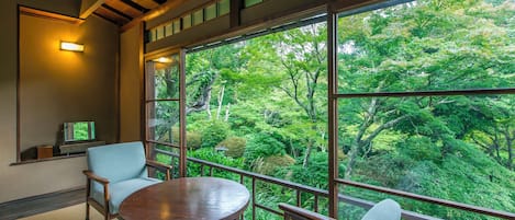 A room with a large window, a round table, two chairs, and a television on a shelf.