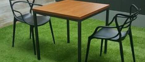 A small outdoor seating area with a wooden table and four chairs, surrounded by artificial grass.