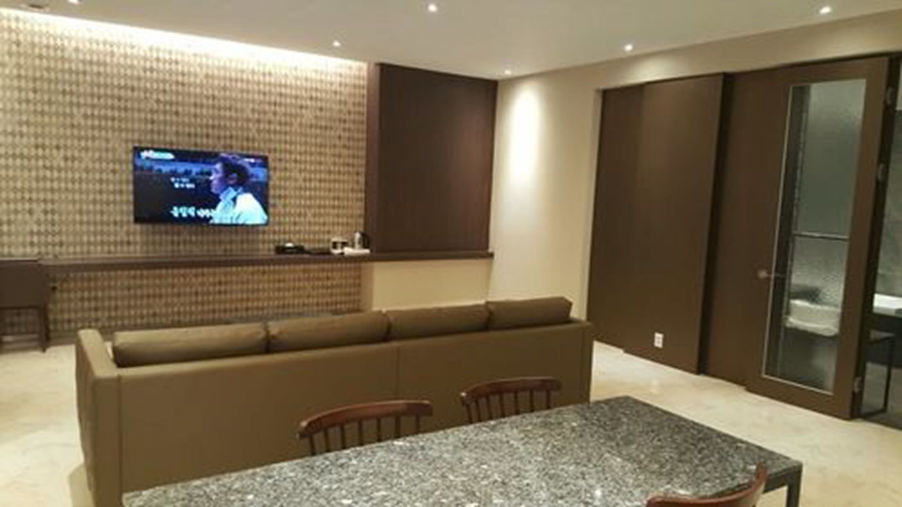 A modern living room with a large sofa, a dining table, and a flat-screen TV mounted on the wall.