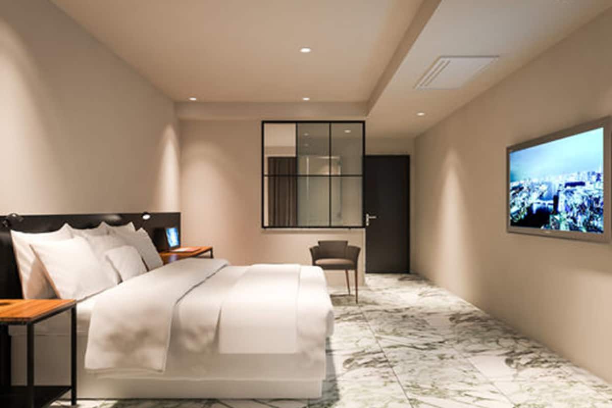 Una habitación de hotel moderna con una cama grande, un escritorio, una silla y una televisión mostrando vistas de la ciudad.