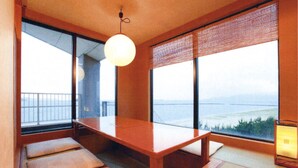 A traditional Japanese room with tatami flooring, a low wooden table, and large windows offering a view of the sea.
