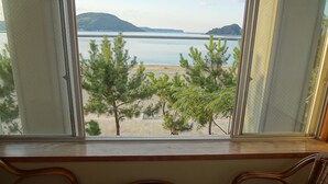 A room with a view of a beach and water, featuring two wicker chairs and a small table.