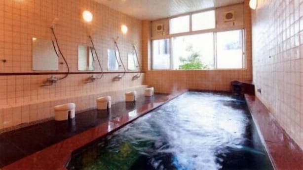 A large indoor swimming pool with a tiled wall, multiple faucets, and a window providing natural light.