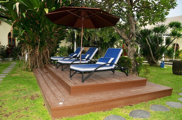 Una terraza de madera con dos sillas reclinables azules y una sombrilla marrón.