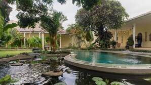 A pool surrounded by tropical plants and a building with a tiled roof. - Villa Costa Sanur (Denpasar)