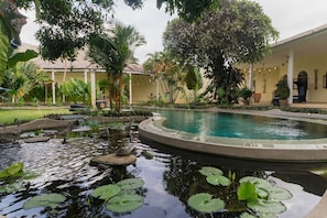 A pool surrounded by tropical plants and a building with a tiled roof. - Villa Costa Sanur (Denpasar)