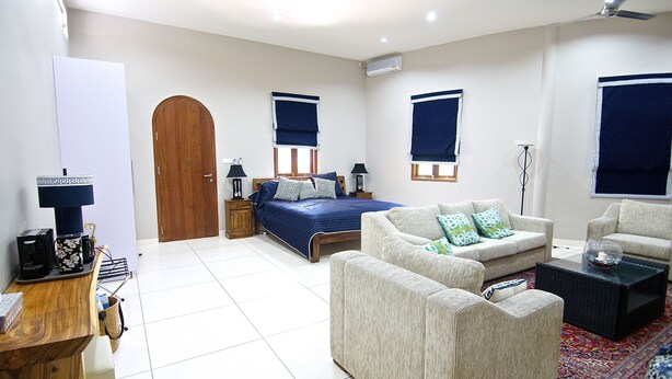 Quarto bem iluminado com cama, dois sofás, uma mesa de centro e uma escrivaninha com computador.