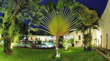 A well-lit outdoor area with a pool, palm trees, and a building with arched windows.
