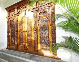 Una puerta de madera grande y ornamentada, con tallas intrincadas y una cruz en la parte superior.
