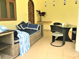 A wicker sofa with a striped blanket, a dining table with chairs, and a potted plant.