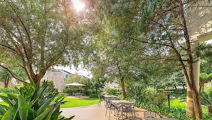 An outdoor patio area with tables and chairs, surrounded by lush greenery and trees. - Garden Court Sandton City (Sandton)