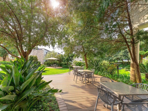 An outdoor patio area with tables and chairs, surrounded by lush greenery and trees. - Garden Court Sandton City (Sandton)
