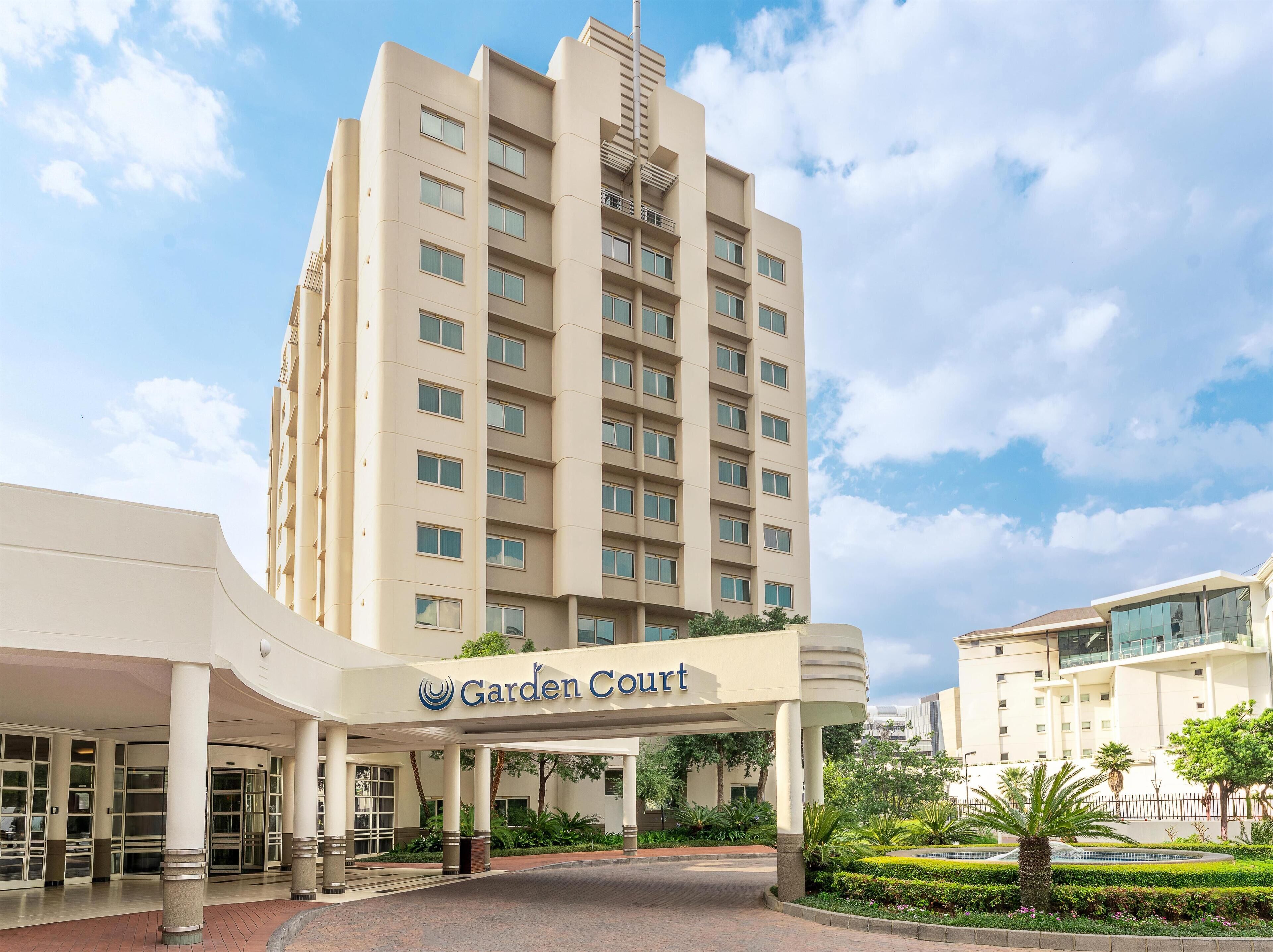 Un hotel con un llamativo letrero que dice 'Garden Court', que presenta un diseño arquitectónico moderno con varios pisos y un atrio central.
