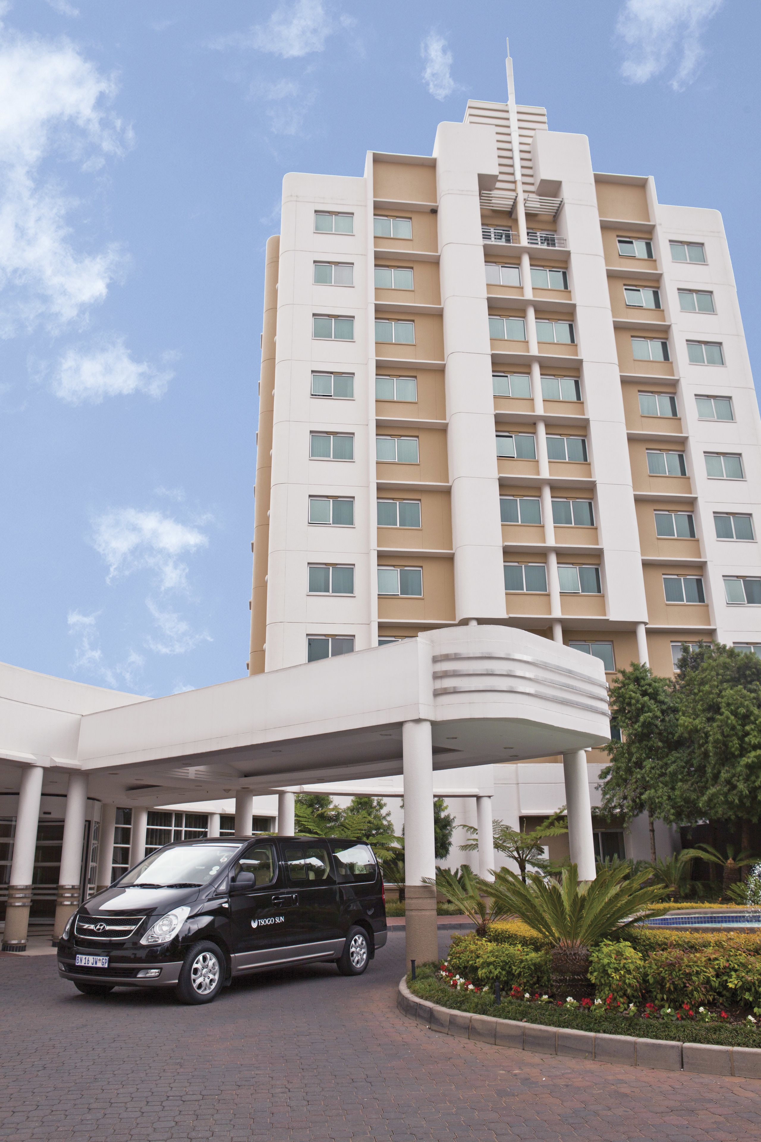 A multi-story hotel with a modern design, featuring a covered entrance and a parking area.