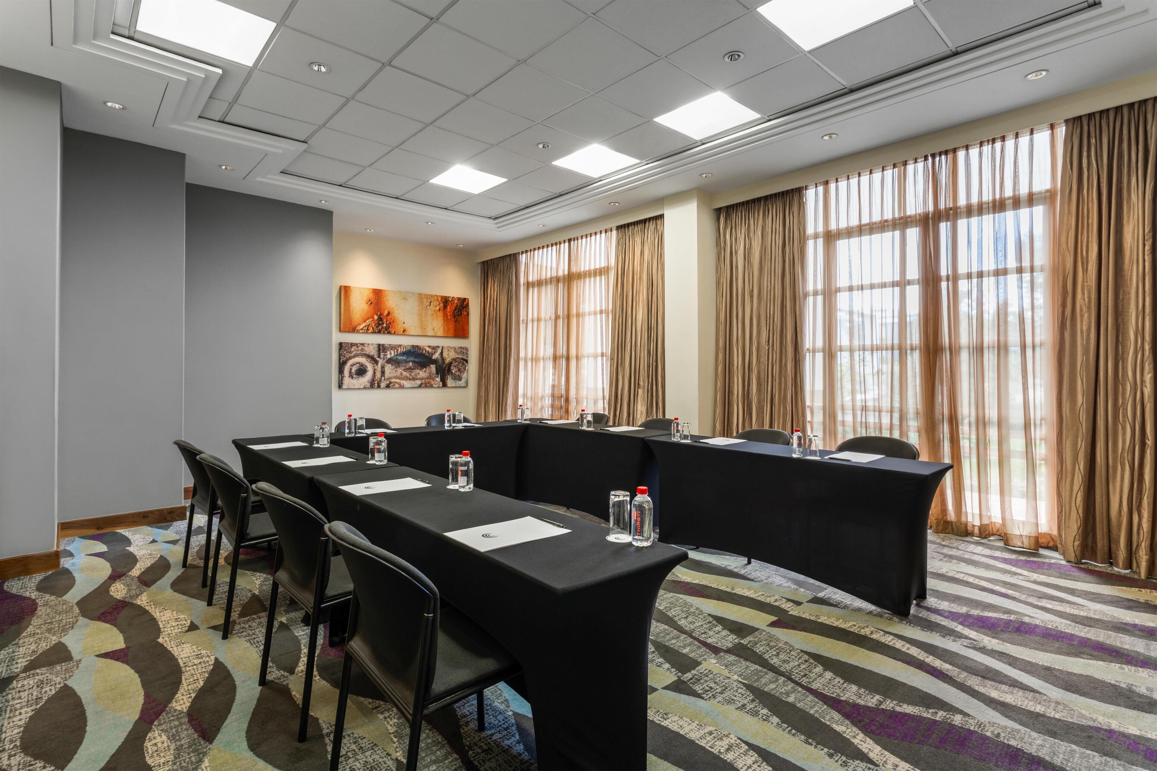 A conference room with a long table, chairs, and a large window with curtains.
