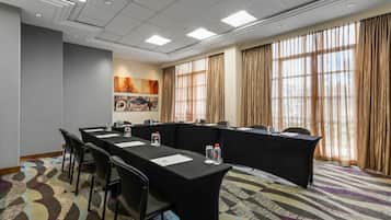 A conference room with a long table, chairs, and a large window with curtains.