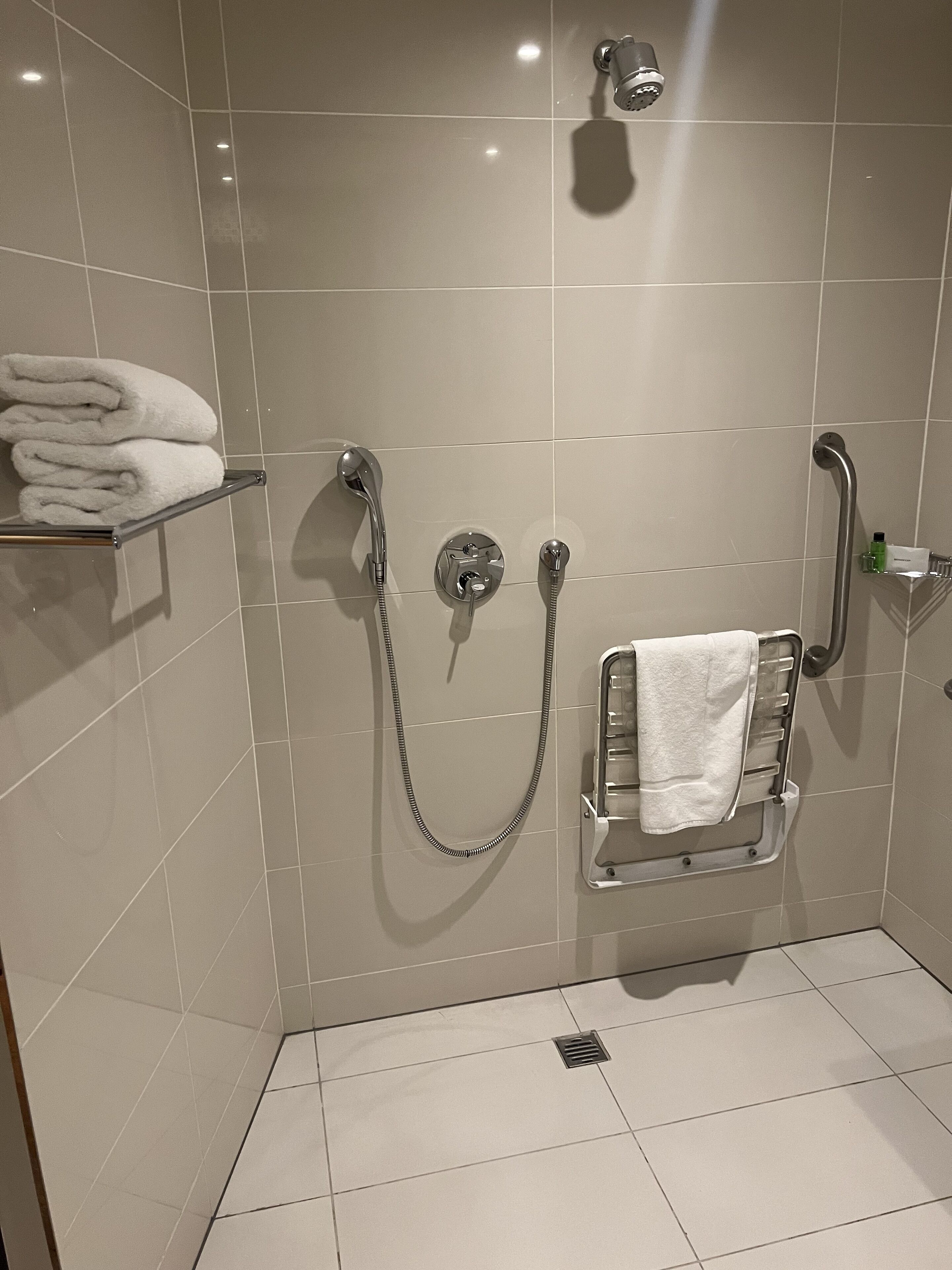 A shower area with a grab bar, a towel rack, and a shelf with folded towels.