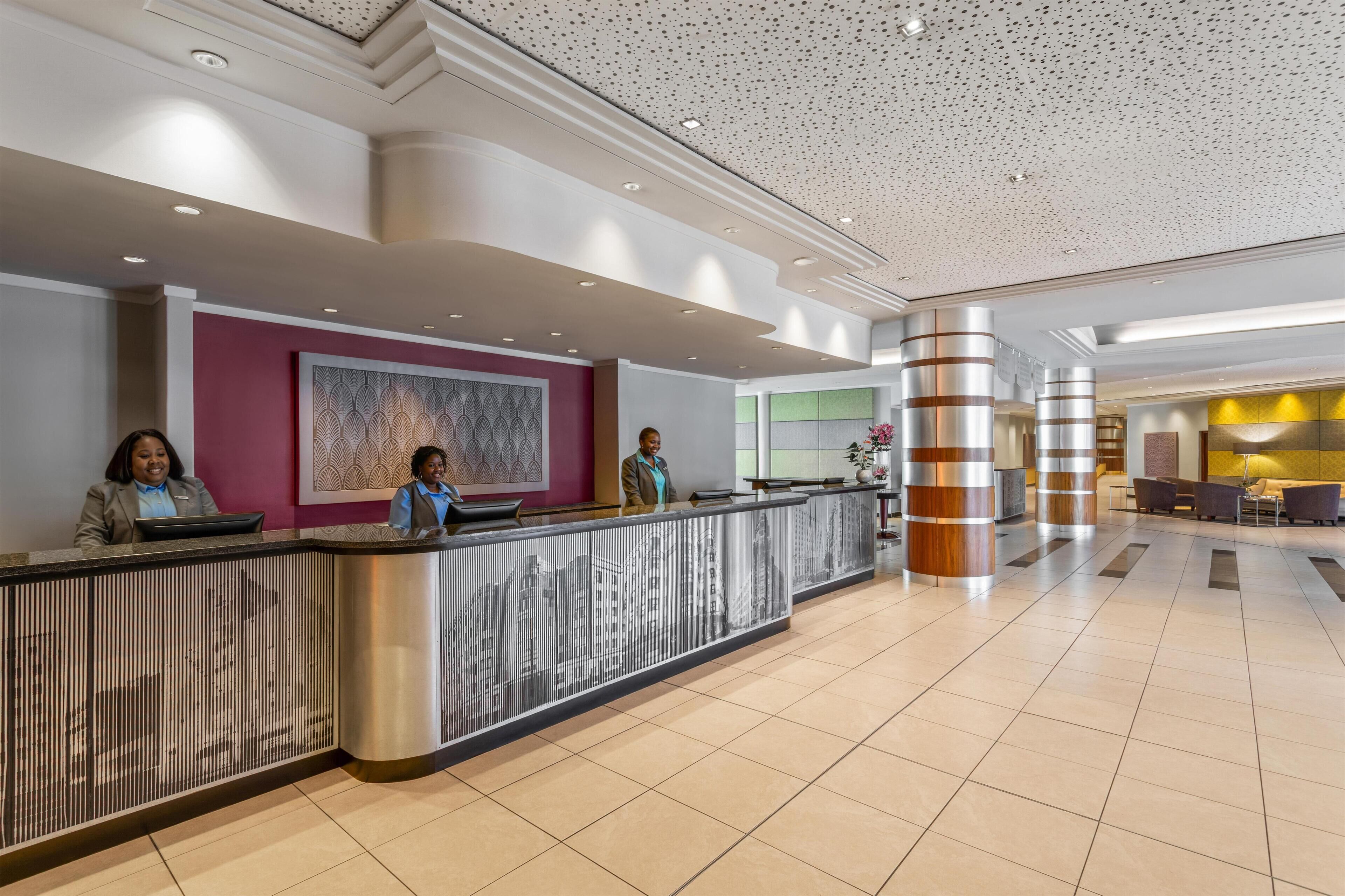 Een moderne hotel lobby met een receptiebalie, een groot abstract schilderij en een zithoek met banken en een salontafel.