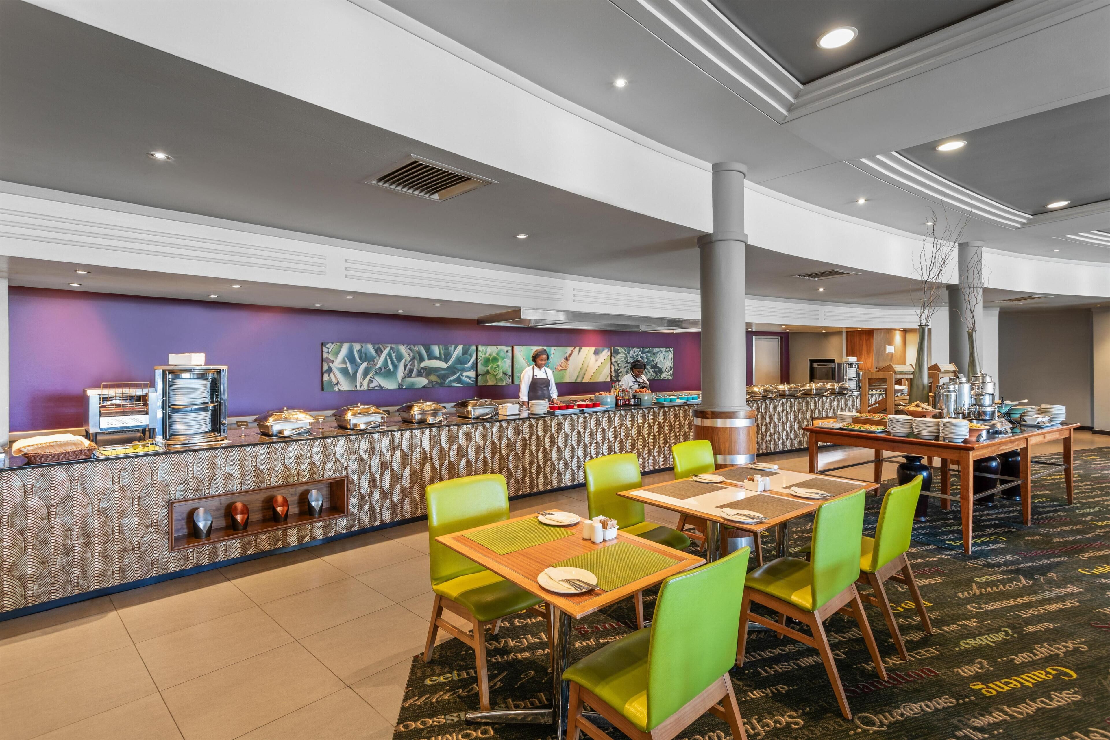 En restaurant i et hotel med buffet, grønne stole og en stribet væg.