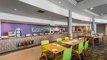 Un comedor de hotel con barra libre, sillas verdes y pared con diseño.