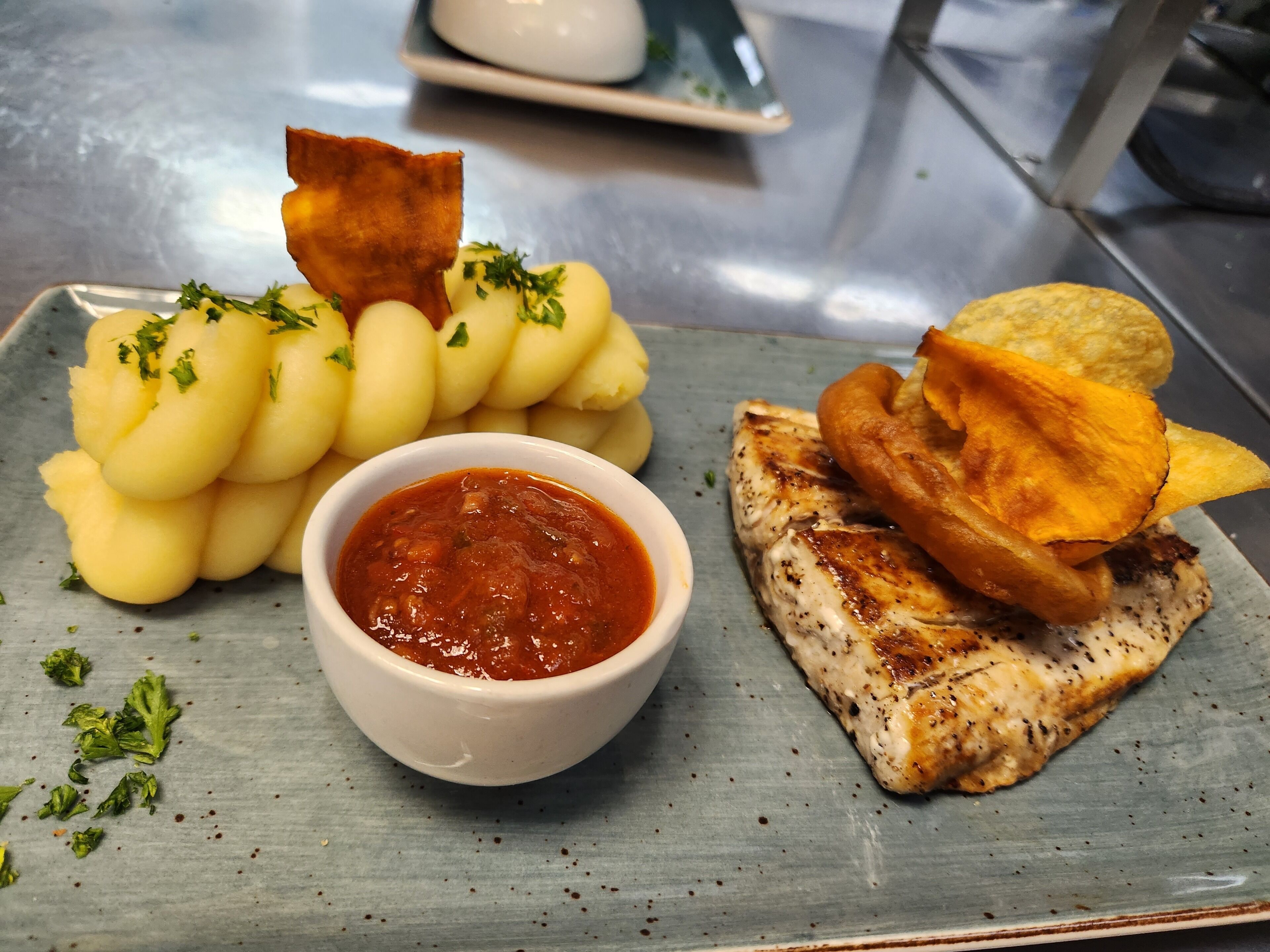 A plate of food with boiled potatoes, a piece of grilled chicken, fried potatoes, and a bowl of sauce.