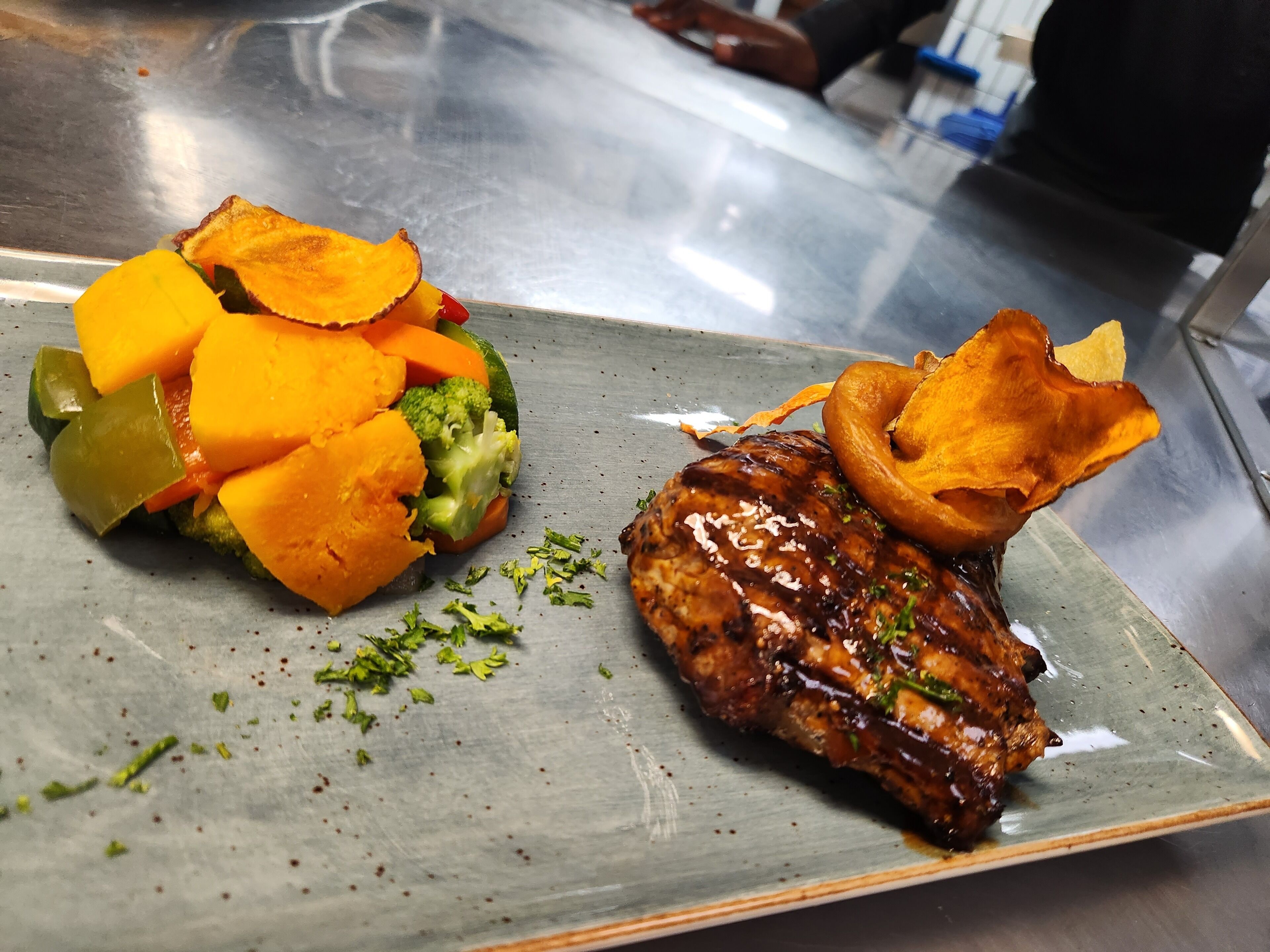 A plate with grilled meat, roasted vegetables, and a side of chips.