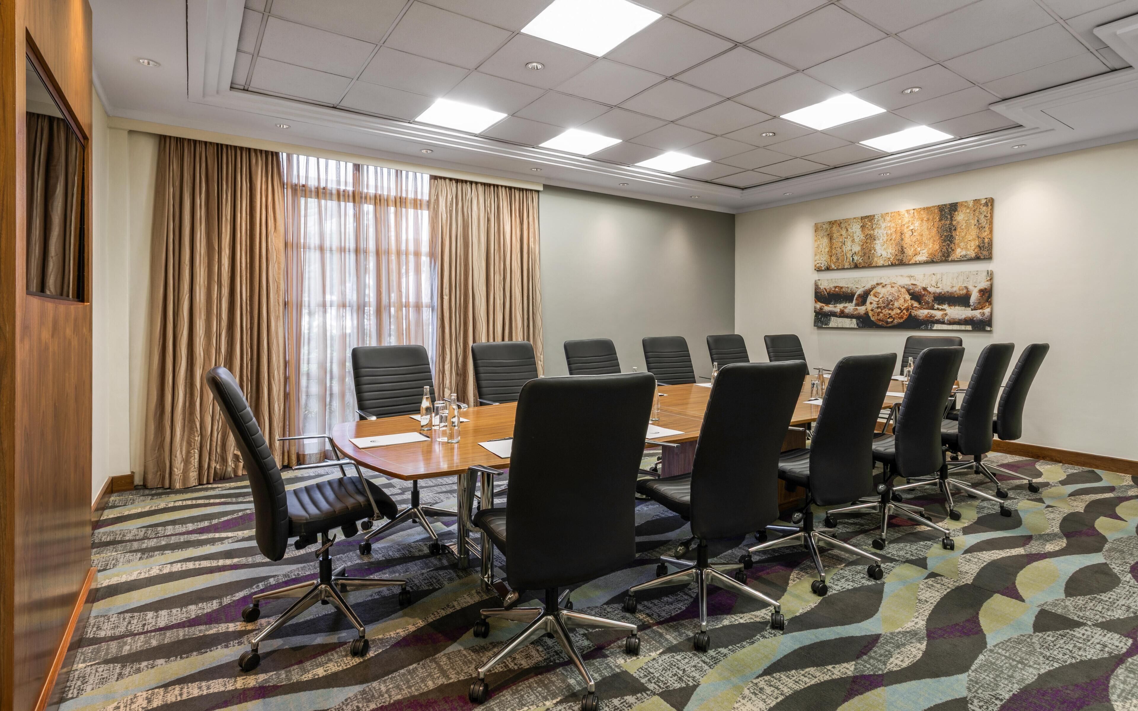 A conference room with a large table, black chairs, a patterned carpet, and a painting on the wall.