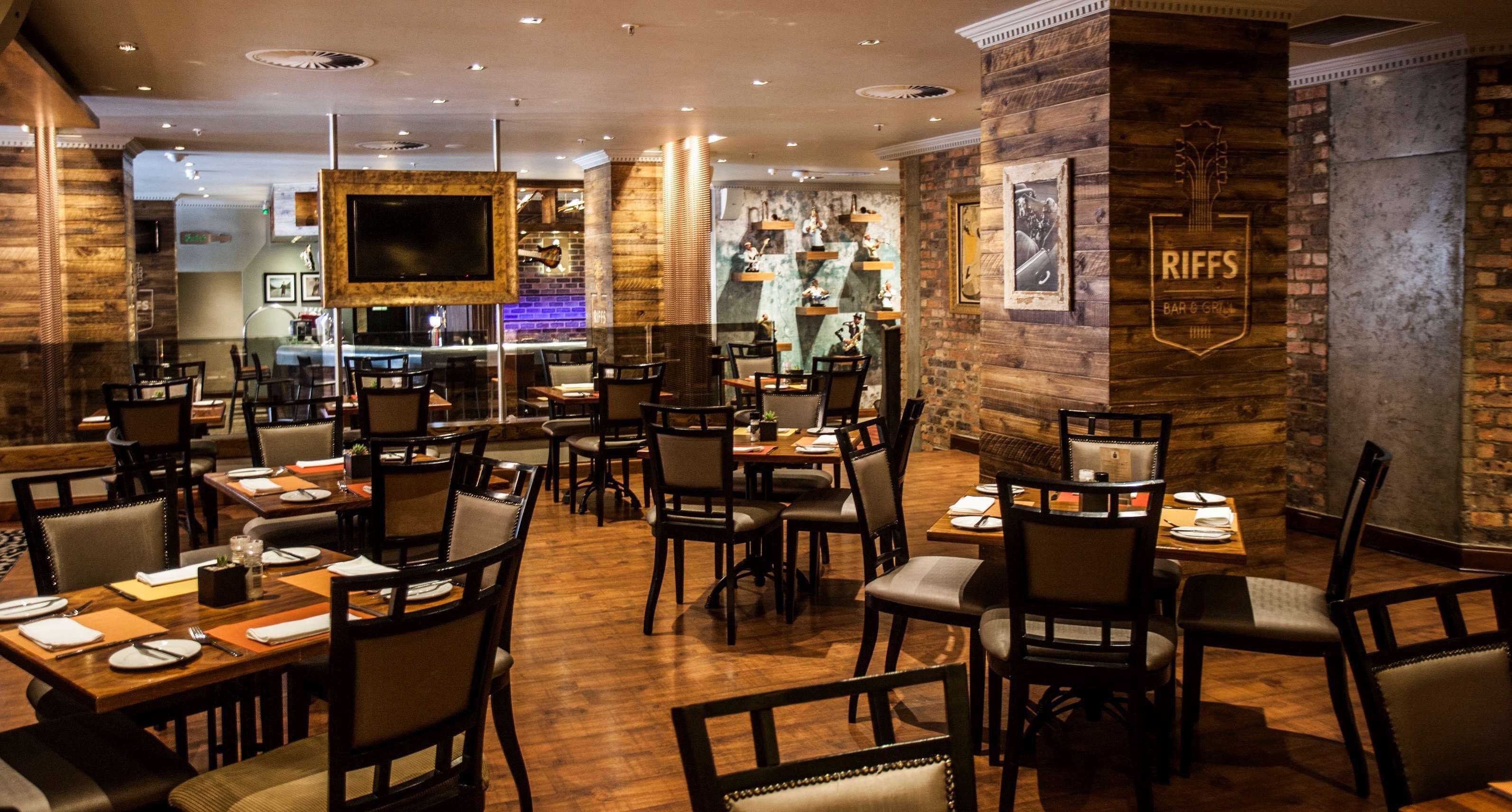 A restaurant with wooden flooring, multiple tables and chairs, a bar area, and a mounted television.