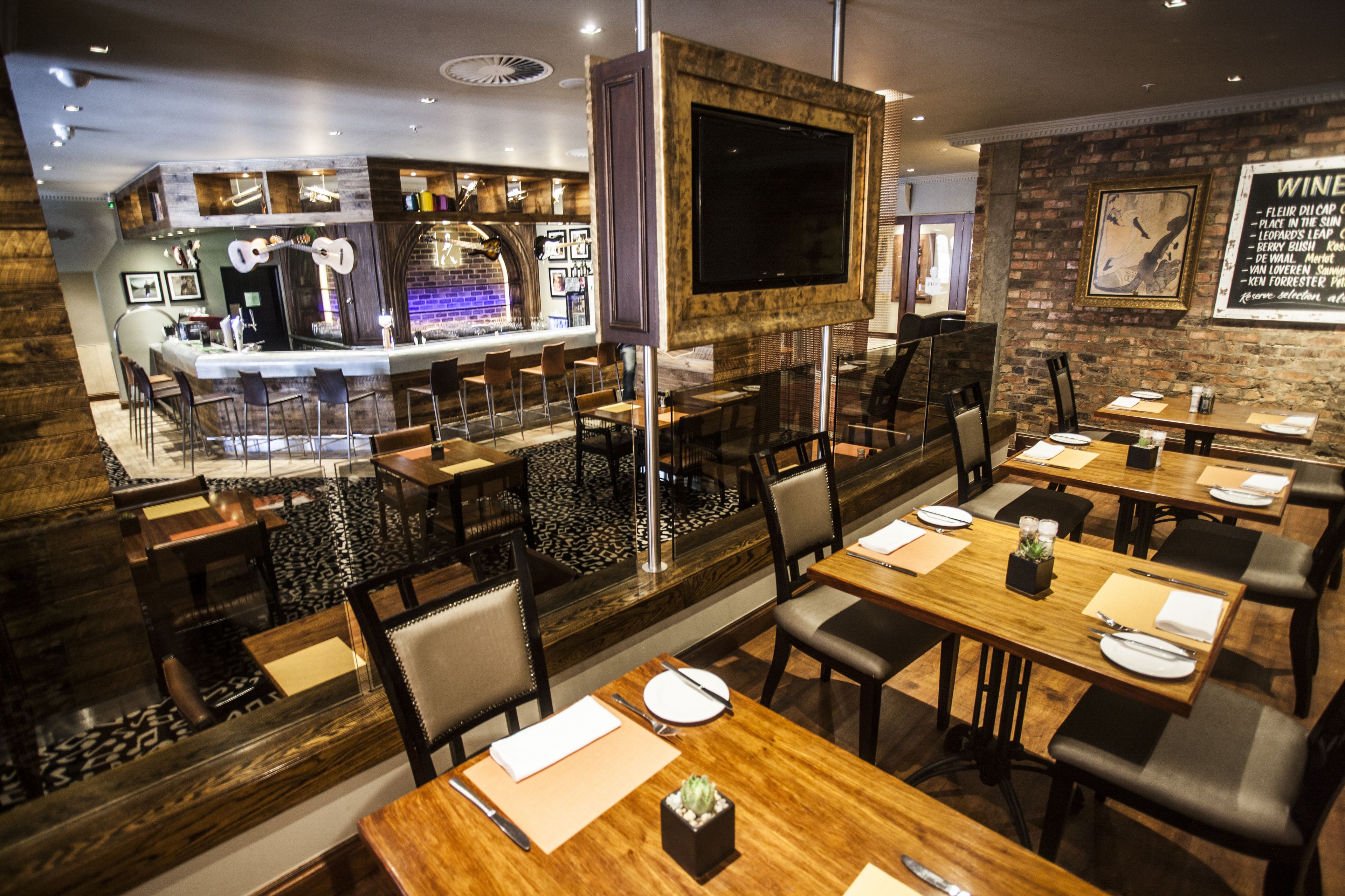 A restaurant with a bar area, wooden tables, and chairs.