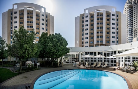 A hotel with a swimming pool, outdoor seating, and two tall buildings in the background.