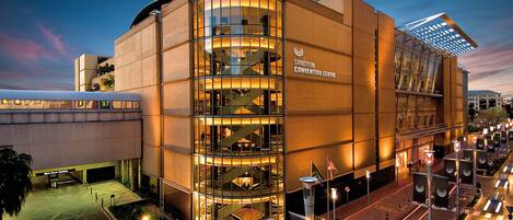 A modern building with a glass facade, labeled "Sandton Convention Centre," featuring a central staircase and multiple levels.