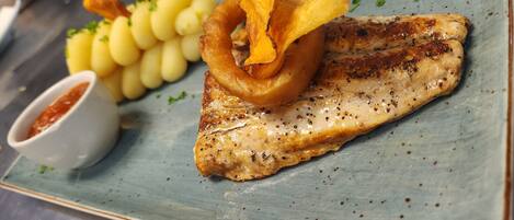 Un plato con pescado a la parrilla, papas fritas y un tazón pequeño de salsa.