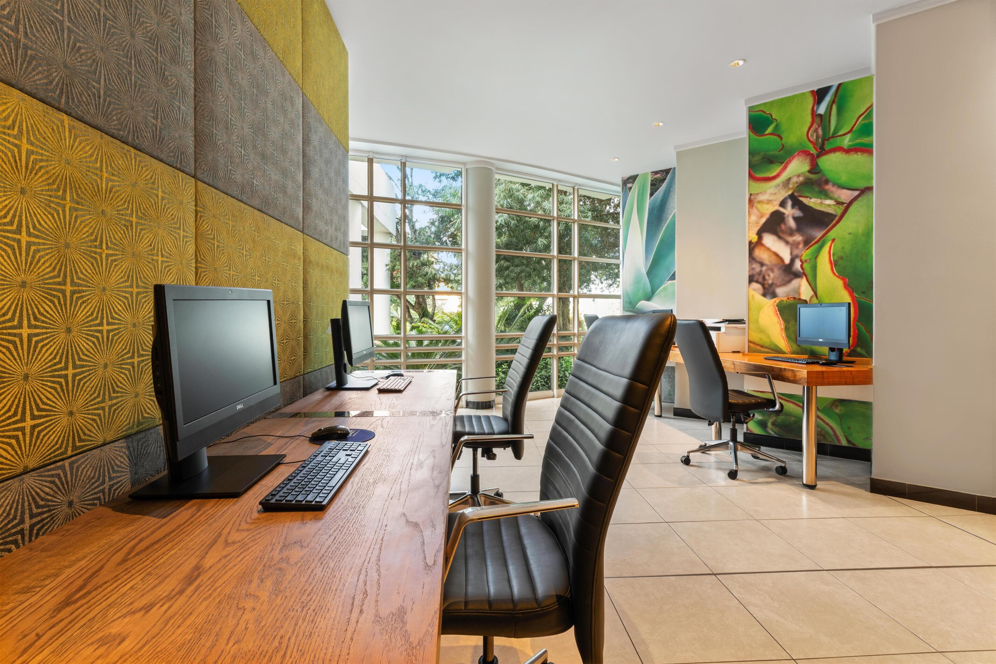 An office space with a wooden desk, two computer monitors, a keyboard, and two office chairs.