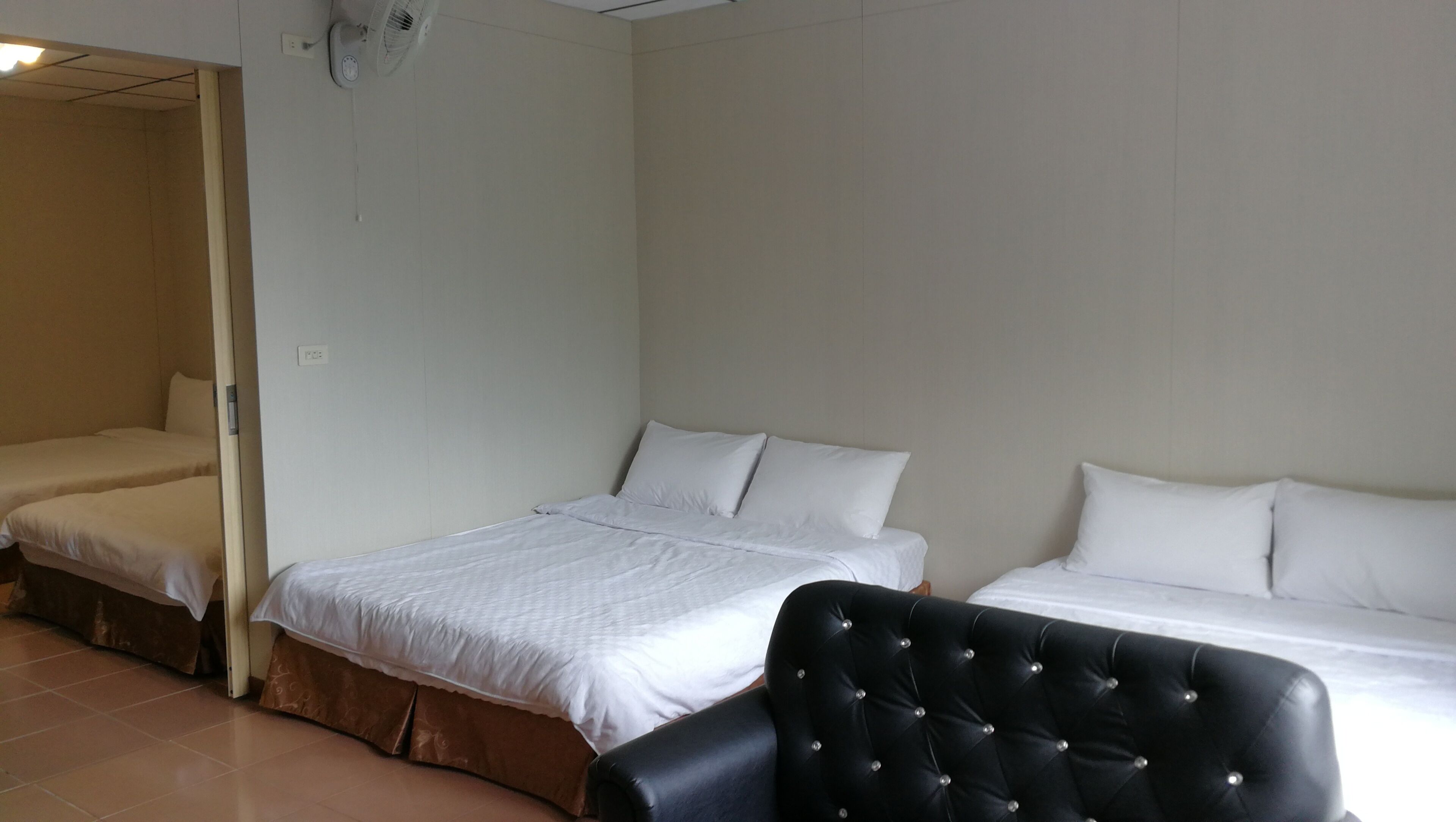 A room with two single beds, a black tufted chair, and a ceiling fan.
