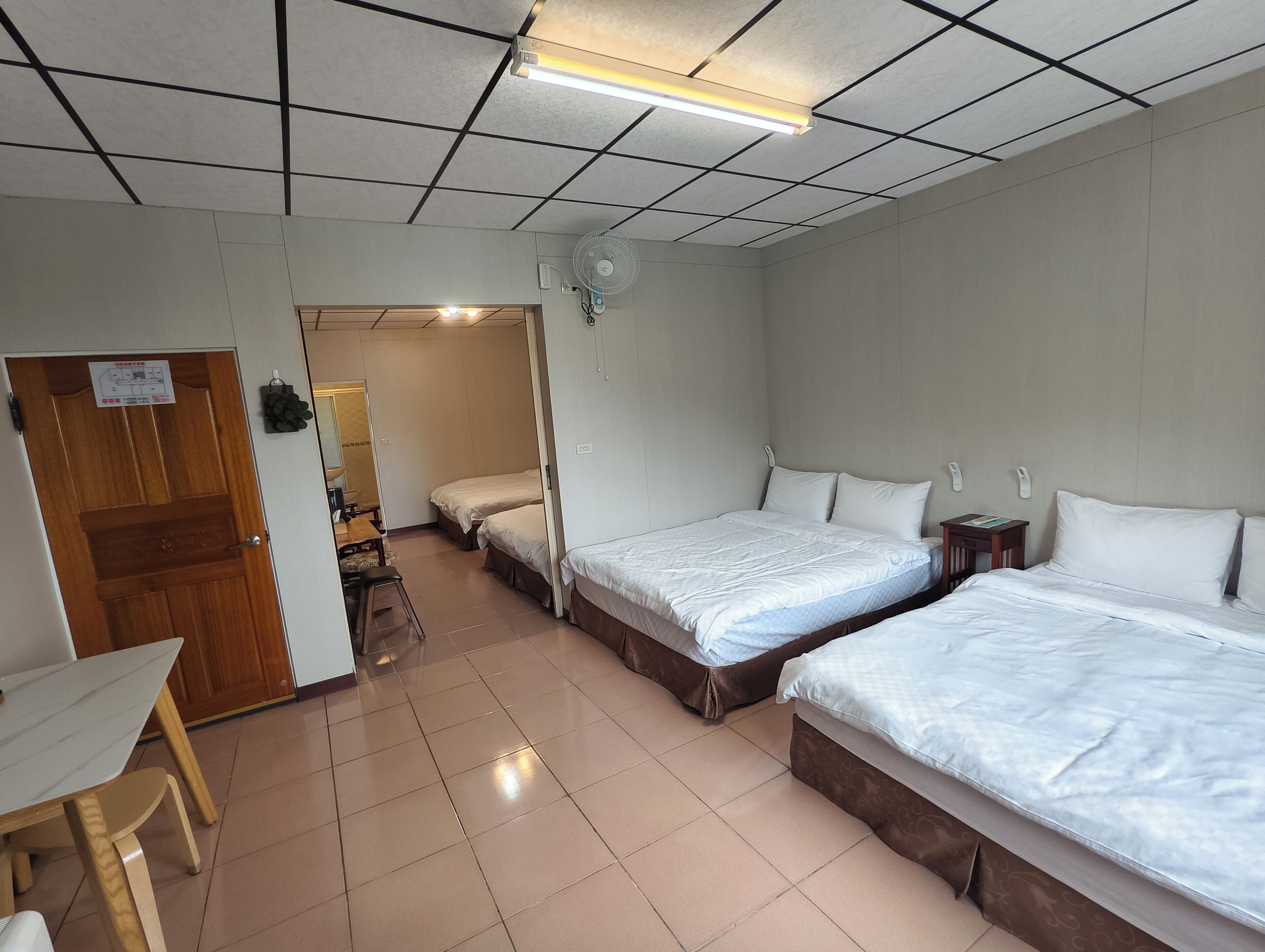 Habitación de hotel con dos camas, un escritorio y una silla. Se ve una puerta que da a un baño y una kitchenette.