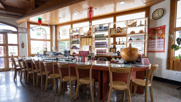 A restaurant with wooden furniture, a large central table, and shelves with various items. - Alishan Tea Homestay (Alishan)