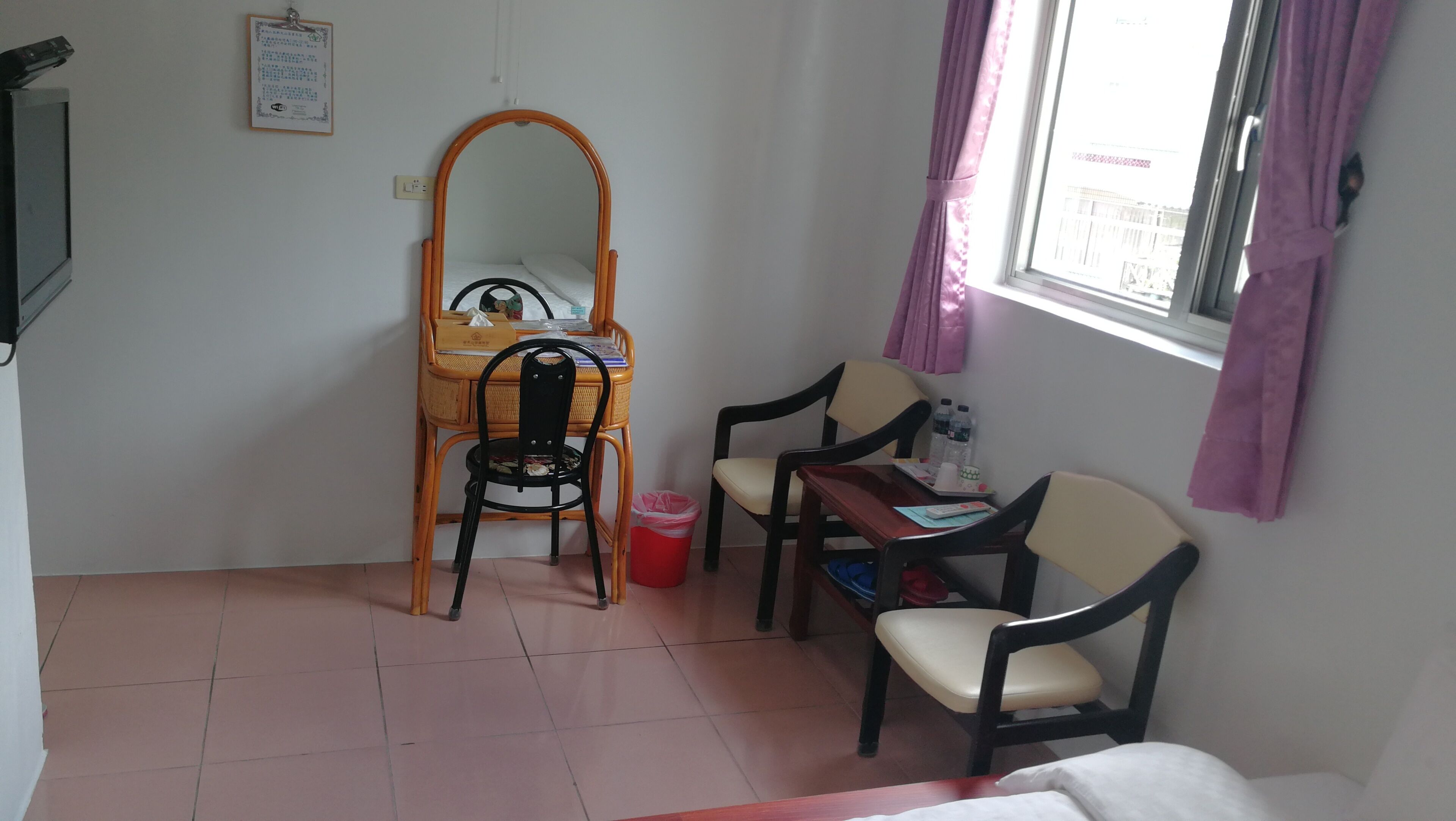 A small room with a wooden chair, a wooden table, a mirror, and a window with curtains.
