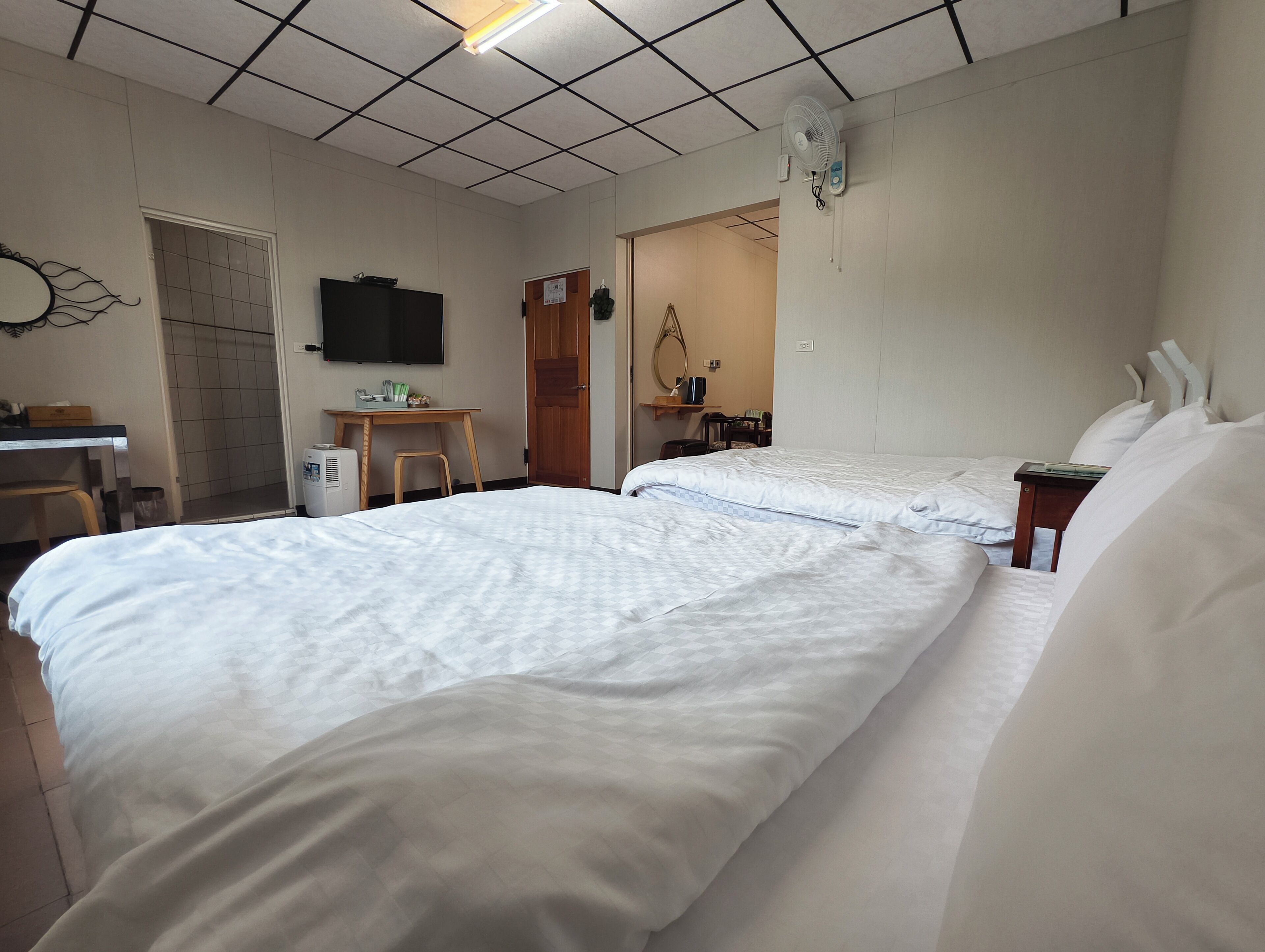 A hotel room with two beds, a desk, a chair, a television, and a door leading to another room.